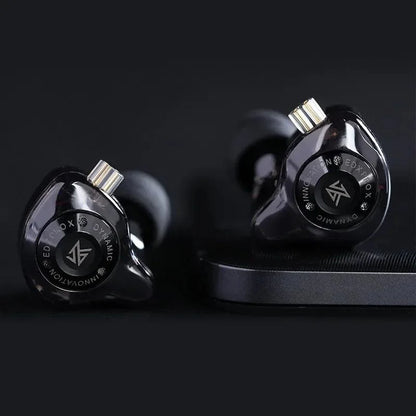 Close-up shot of Black KZ EDX Pro X earphones on a dark surface, highlighting star‑style faceplate and cable wrap.